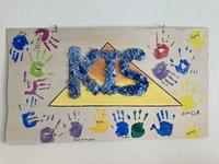 Holzschild mit den Buchstaben K I S in der Mitte und bunten Handabdrücken von Kindern herum