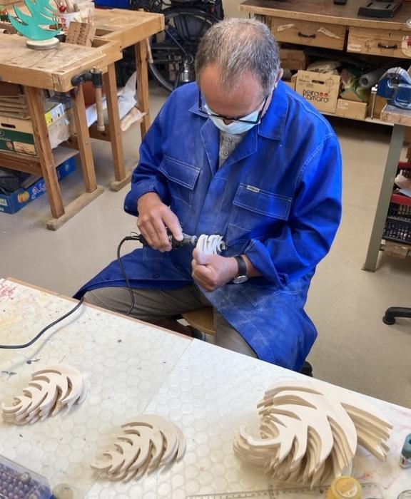 Unser Mitarbeiter Herr Stelle, trägt einen blauen Arbeitskittel bearbeitet Holz in unserer Werkstatt.