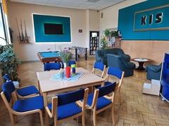 Raum mit Tischgruppe und Sofaecke zum Verweilen, großer Fernseher vor türkisgestrichener Wand
